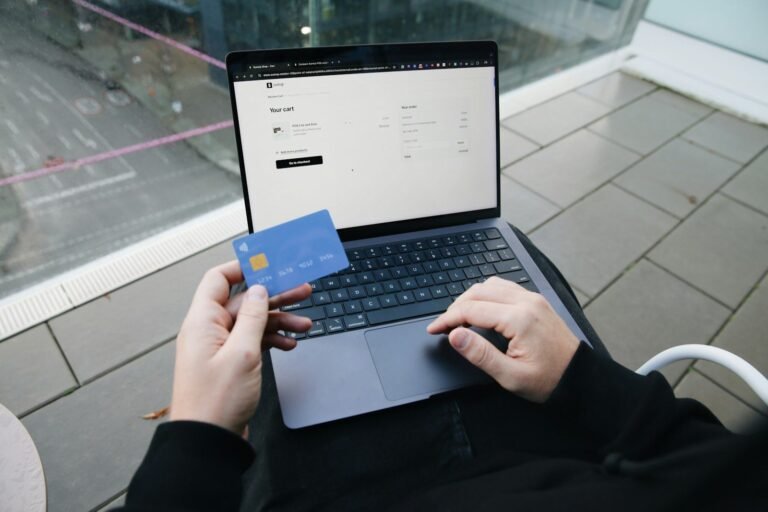 Person holding a blue card while typing on a laptop showing an online checkout form