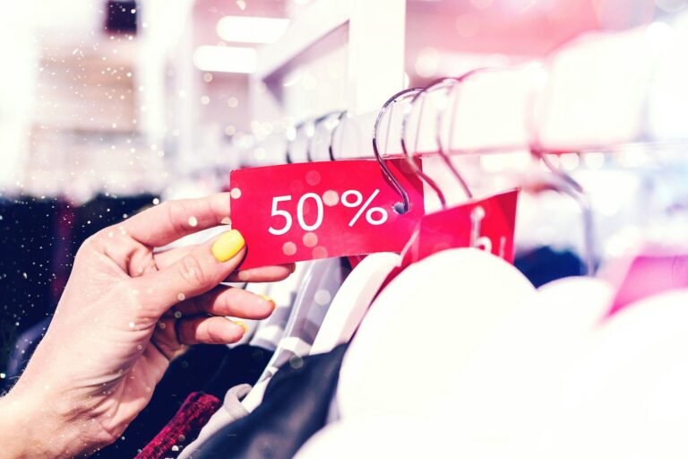 Hand holding a red 50 percent discount price tag attached to clothes on a store rack